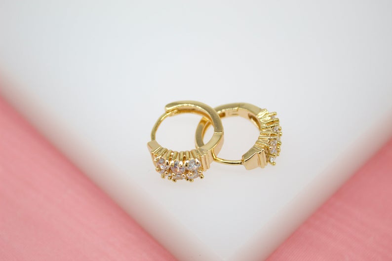 A pair of sparkling gold hoop earrings with crystal embellishments rest on a soft white surface.