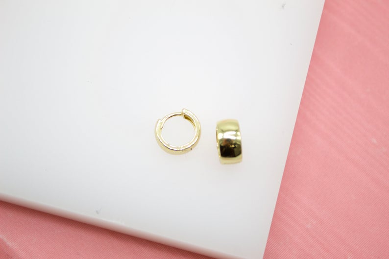 A pair of sleek gold huggie hoop earrings rests on a white display surface.
