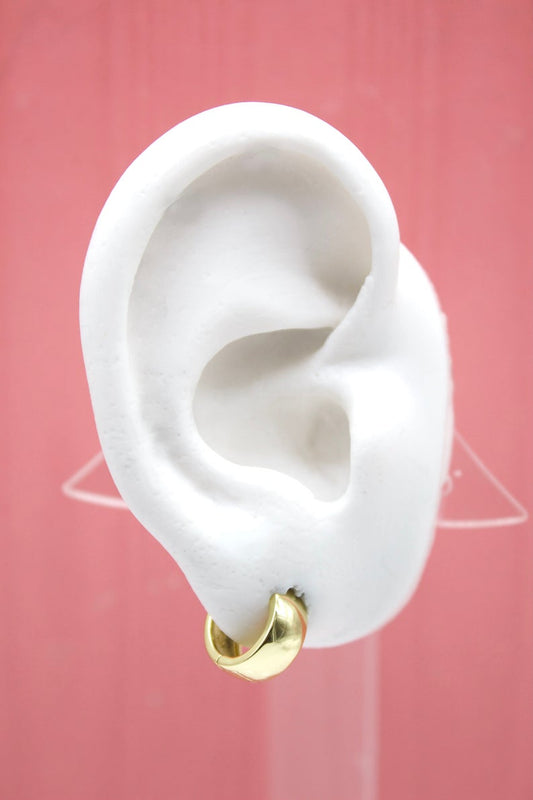 A white mannequin ear displays a small gold hoop earring against a pink background.