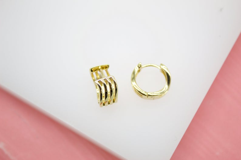 A pair of polished gold multi-row huggie hoop earrings rests on a clean white surface.