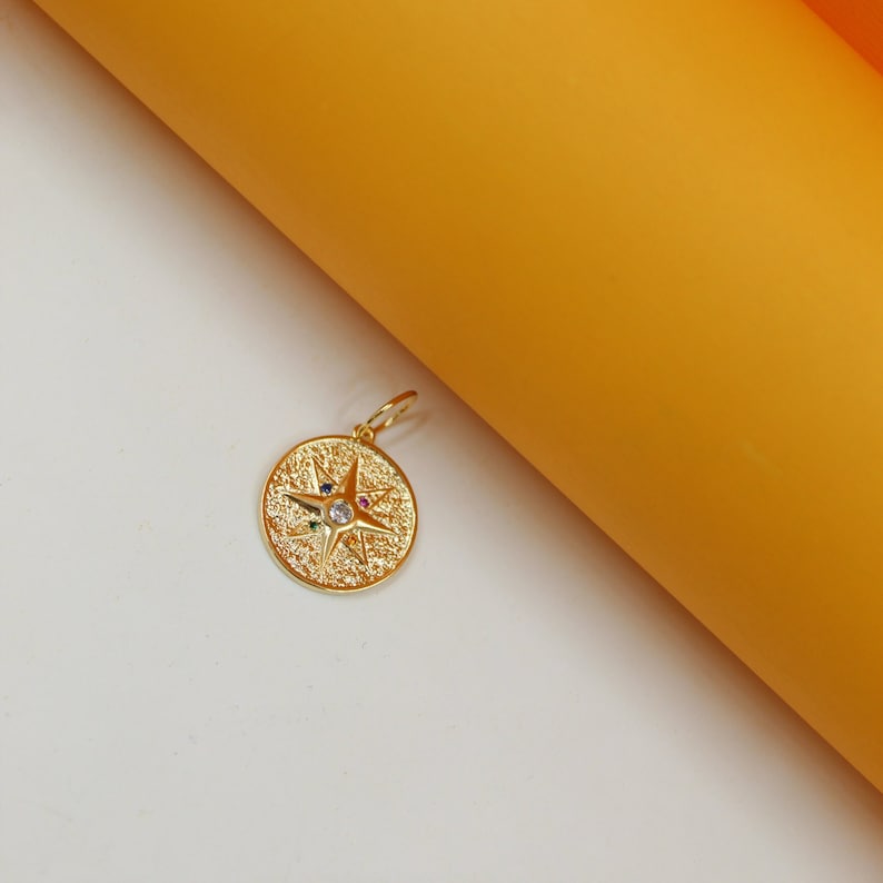 A gold pendant featuring a textured compass star design rests against a white and yellow backdrop.