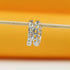 Two silver chain-link hoop earrings hang from a wooden stick against a bright orange background.