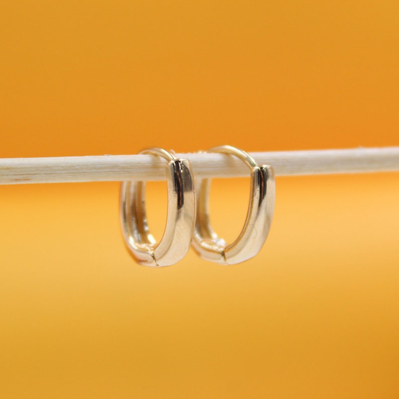 Two polished gold hoop earrings hang delicately from a thin white stick against a vibrant yellow background.