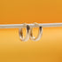 Two polished gold hoop earrings hang delicately from a thin white stick against a vibrant yellow background.