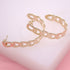 A pair of gold chain link hoop earrings rests on a soft pink surface.