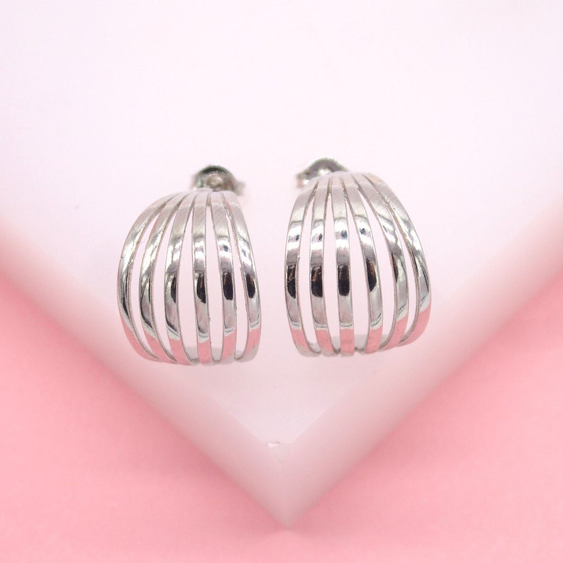 A pair of polished silver multi-band hoop earrings rests on a pink and white surface.