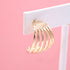 A gold multi-strand hoop earring hangs from a white display card against a soft pink background.