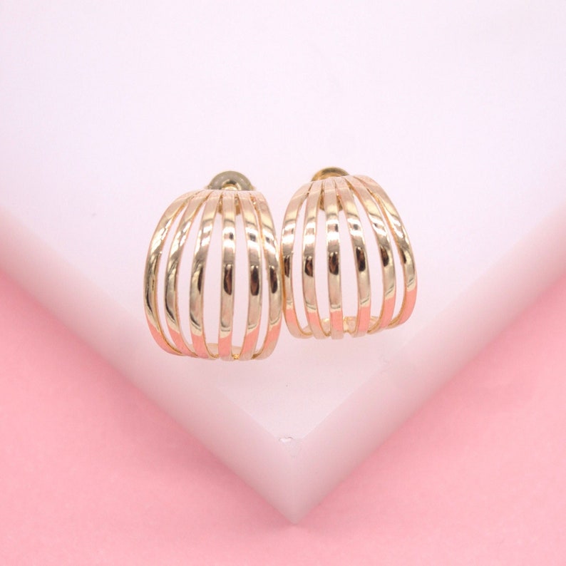 A pair of elegant multi-band gold hoop earrings rests upright on a light pink and white display stand.