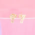 A pair of delicate gold clothespin-shaped stud earrings rests upright on a soft pink surface.