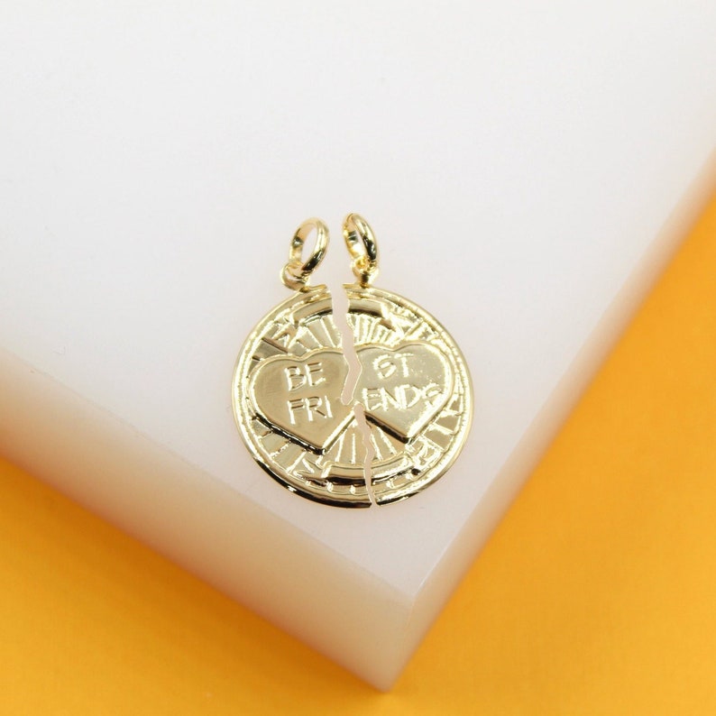 A gold best friends broken heart pendant rests on a white surface against an orange background.