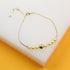A delicate gold chain bracelet features a central arrangement of alternating pearls and a polished gold bead resting on a white display block.
