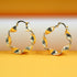 A pair of shiny gold twisted hoop earrings rests on a gradient orange and white surface.