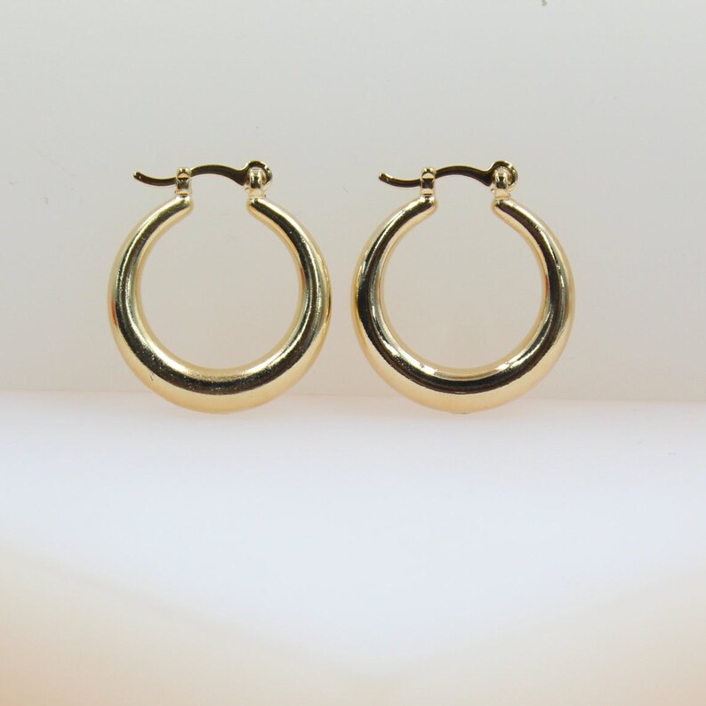A pair of polished gold hoop earrings rests neatly on a clean white surface.