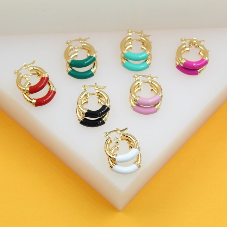 Several pairs of colorful enamel gold hoop earrings are neatly arranged on a white display stand.