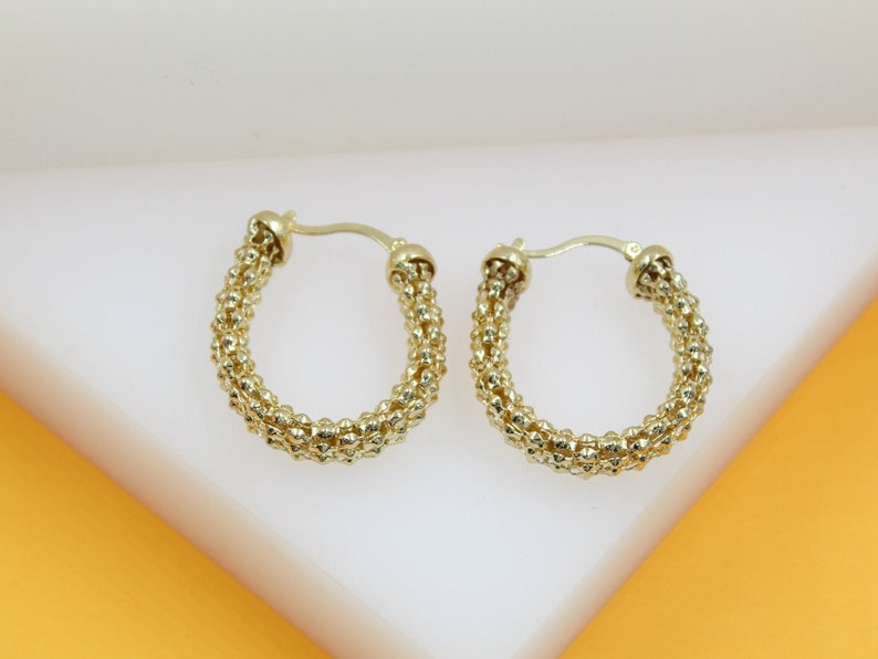 A pair of textured gold hoop earrings rests on a clean white surface.