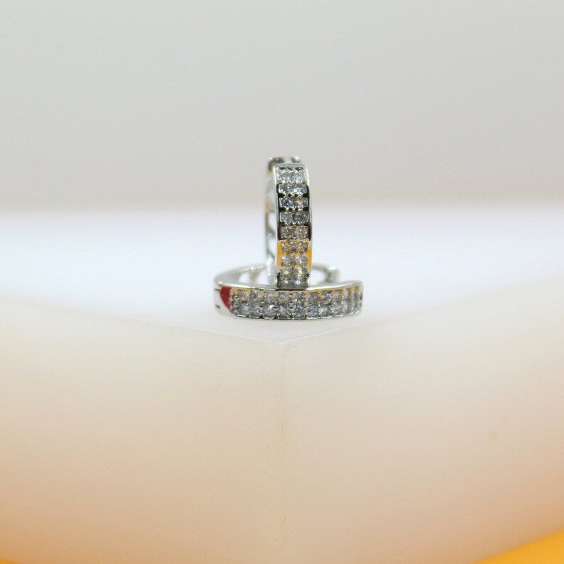 A pair of silver hoop earrings encrusted with sparkling cubic zirconia stones rests on a white display surface.