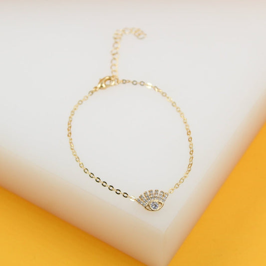 A delicate gold chain bracelet features a sparkling evil eye pendant encrusted with cubic zirconia stones.