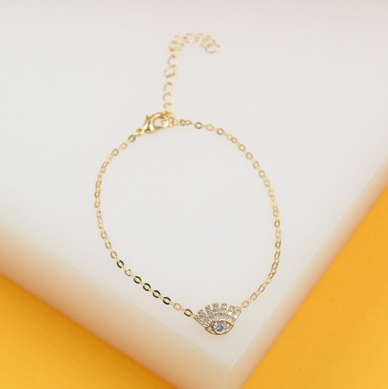 A delicate gold chain bracelet features a sparkling evil eye charm embellished with cubic zirconia stones.