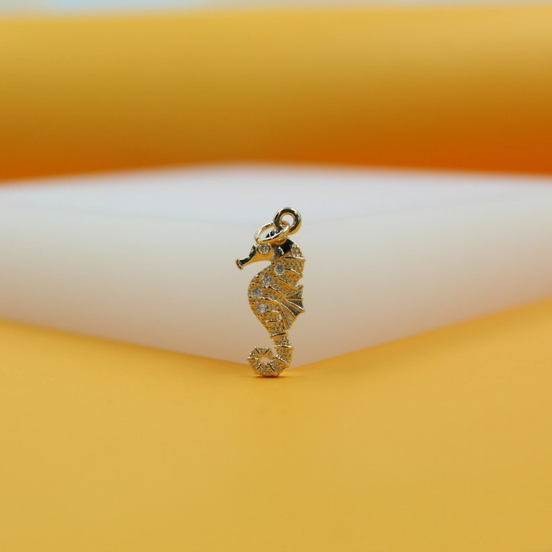 A gold seahorse pendant sparkles with embedded diamonds against a warm yellow and white backdrop.