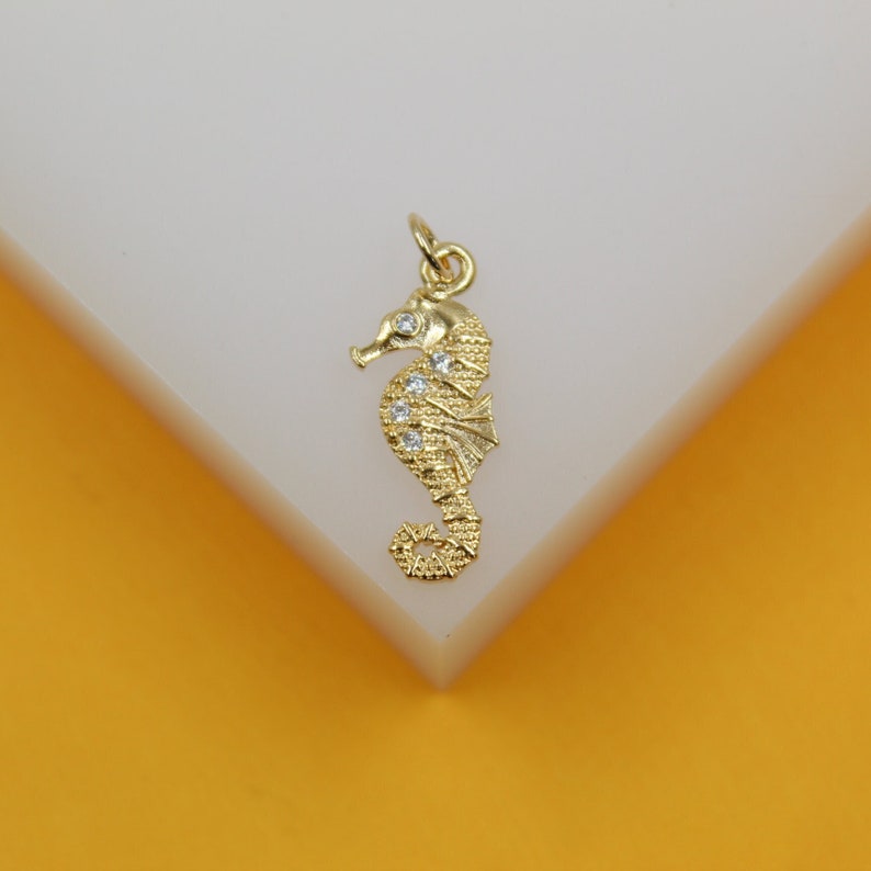 A gold seahorse pendant features sparkling cubic zirconia stones along its back against a light background.