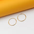 Two polished gold hoop earrings rest on a white surface against a vibrant yellow background.