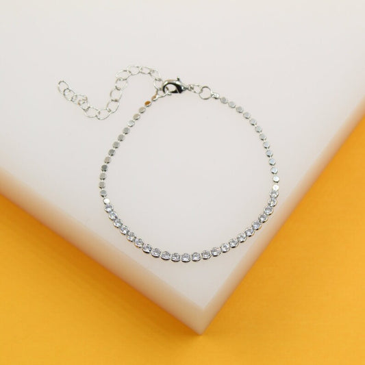 A sparkling silver tennis bracelet with cubic zirconia stones lies on a light-colored display surface.