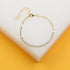 A delicate gold tennis bracelet featuring sparkling cubic zirconia stones rests on a white and yellow display block.