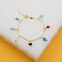 A delicate gold-link charm bracelet displays colorful multi-gemstone beads dangling against a clean white and yellow display surface.