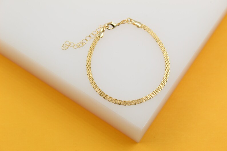 A delicate gold mesh bracelet rests on a white display block against an orange background.