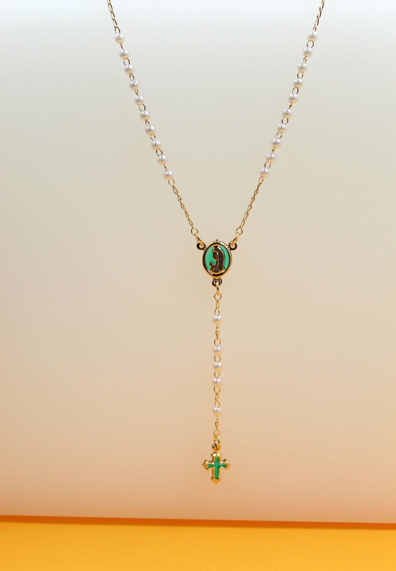A delicate gold rosary necklace features white pearls and a matching green enamel centerpiece and crucifix.