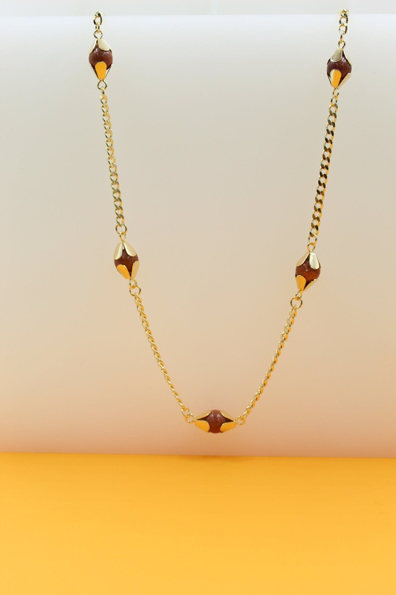 A delicate gold chain necklace features sparkling brown gemstone beads accented with gold settings against a neutral display backdrop.