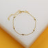 A delicate gold beaded bracelet with textured oval charms lies on a white surface.