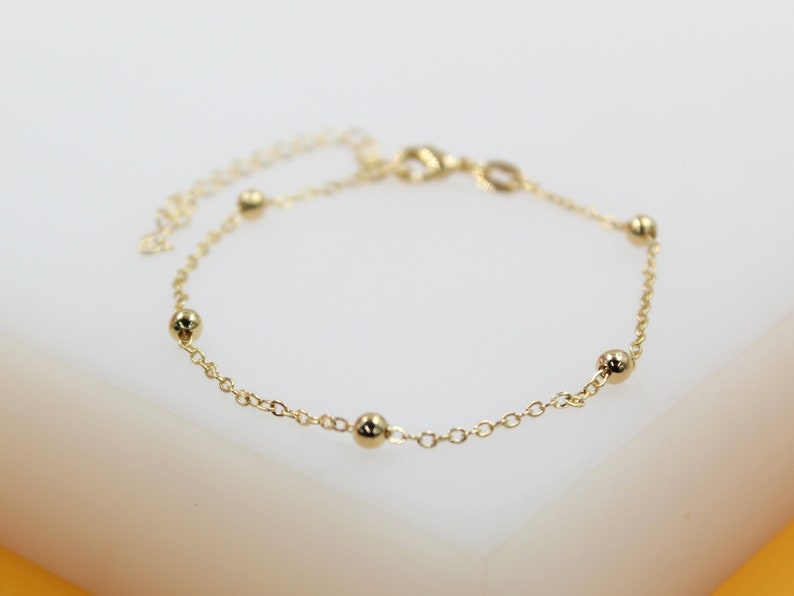 A delicate gold chain bracelet features evenly spaced shiny bead charms against a neutral background.