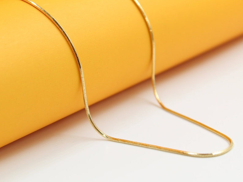 A delicate gold snake chain necklace rests against a vibrant yellow background.