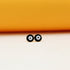 Two round black and white enamel evil eye stud earrings rest side by side against a soft peach and yellow background.