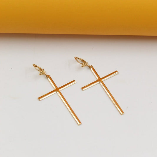 A pair of elegant gold cross earrings rests on a clean white surface against a warm yellow backdrop.