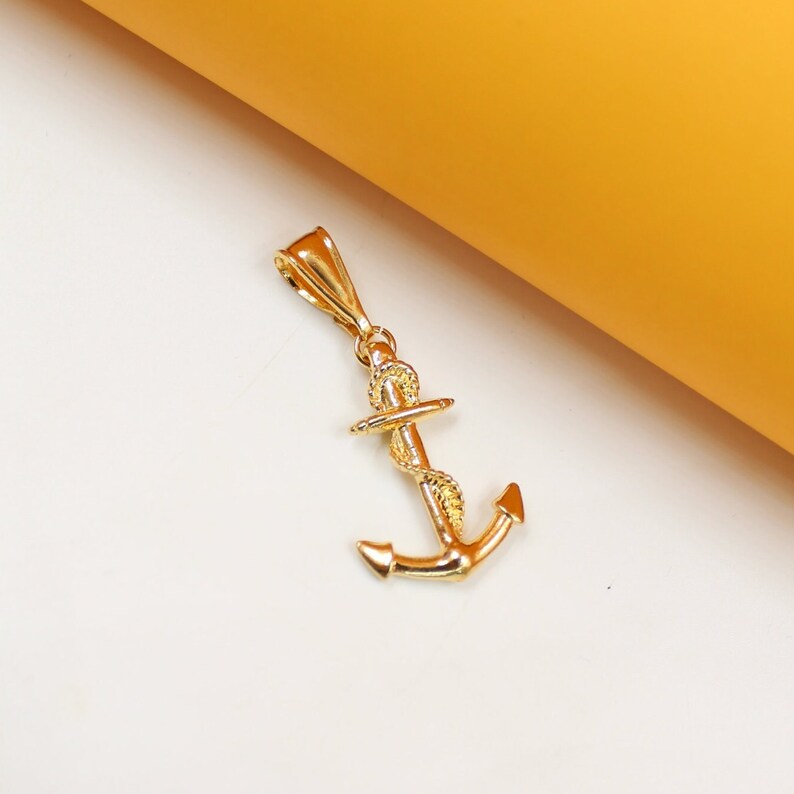 A polished gold anchor pendant rests against a white and yellow background.