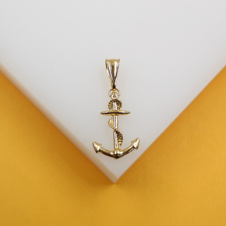 A polished gold anchor pendant rests against a white display block.