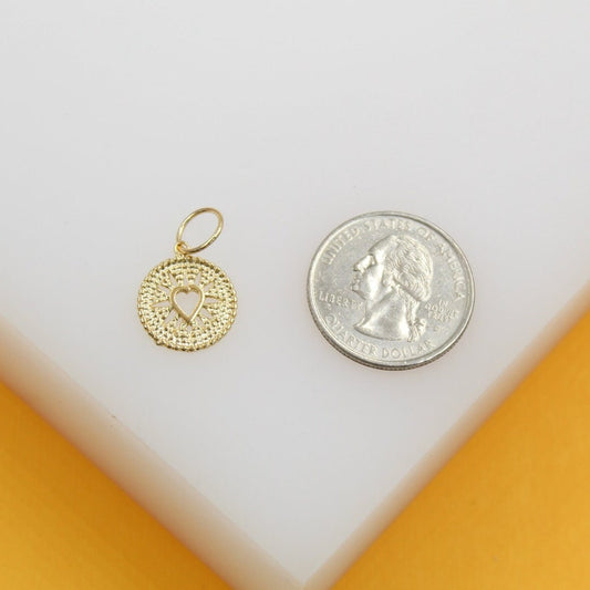 A delicate gold heart charm rests next to a US quarter coin for size comparison on a white surface.