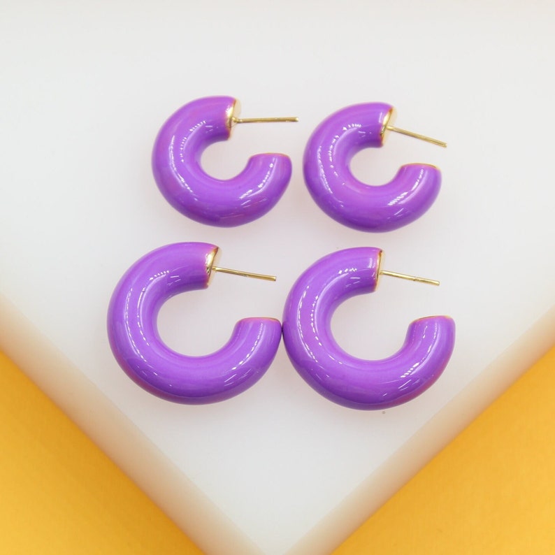 Four shiny purple enamel huggie hoop earrings with gold-tone posts rest on a white display surface.