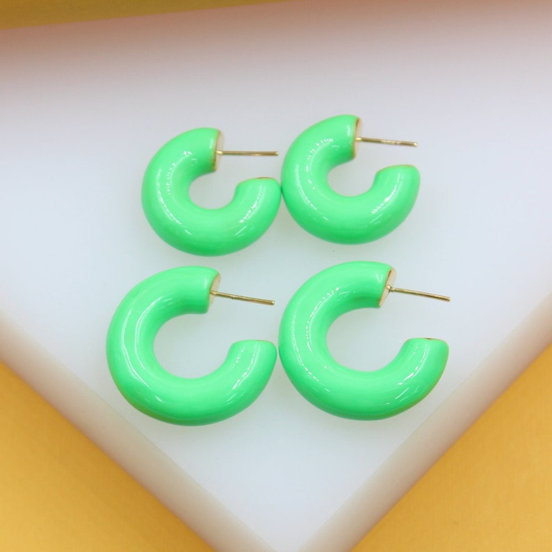 Two pairs of bright neon green enamel hoop earrings rest on a white display surface.