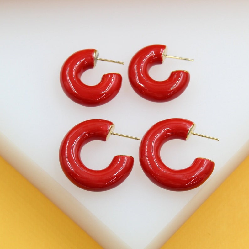 Four glossy red enamel hoop earrings display gold posts against a neutral white and yellow background.