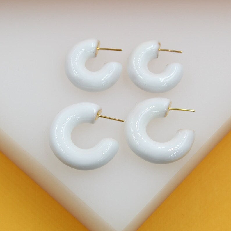 Four white enamel hoop earrings with gold posts rest neatly on a white surface.