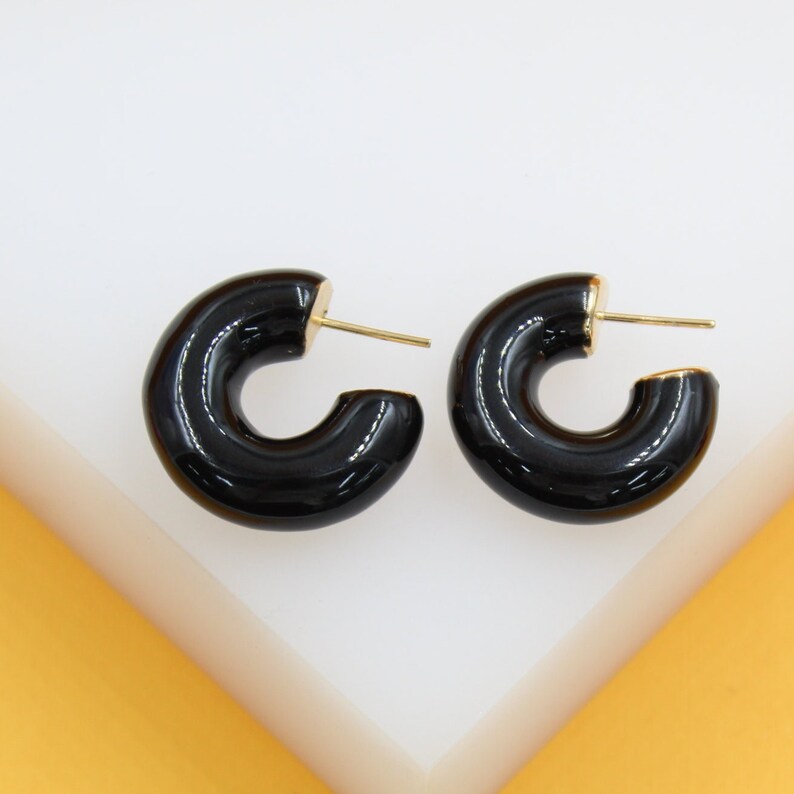Glossy black enamel hoop earrings with gold posts rest on a white surface.