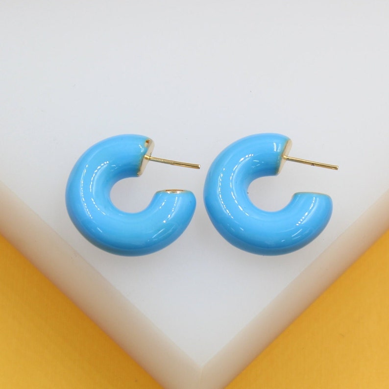 A pair of bright blue enamel hoop earrings rests on a white display stand.