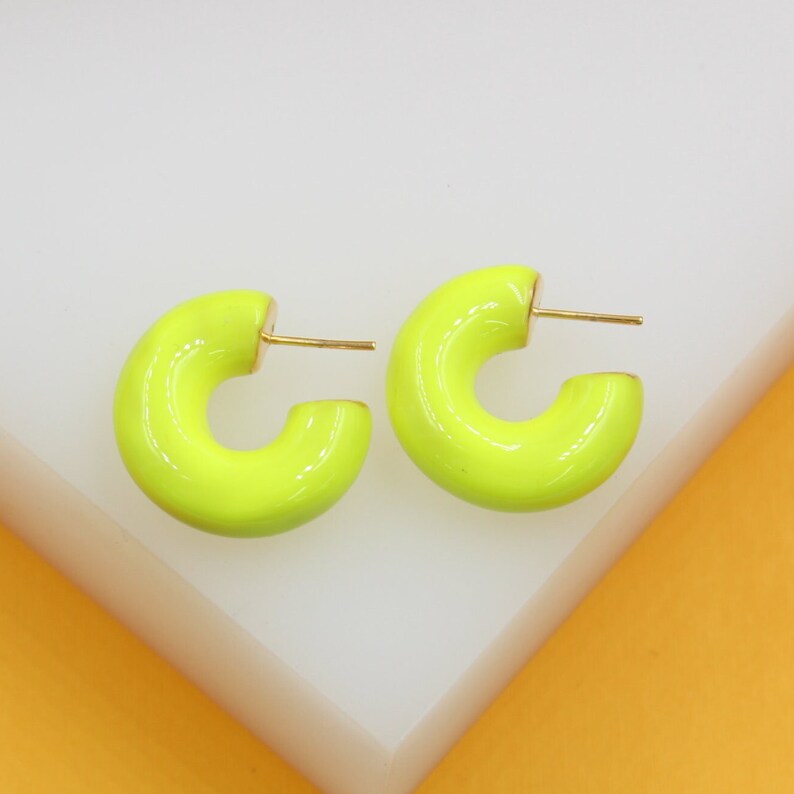 A pair of vibrant neon green enamel hoop earrings rests on a white display block.