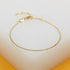 A delicate gold bead chain bracelet rests on a clean white display surface against a warm yellow background.