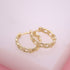 A pair of gold chain link huggie hoop earrings rests delicately on a soft pink surface.
