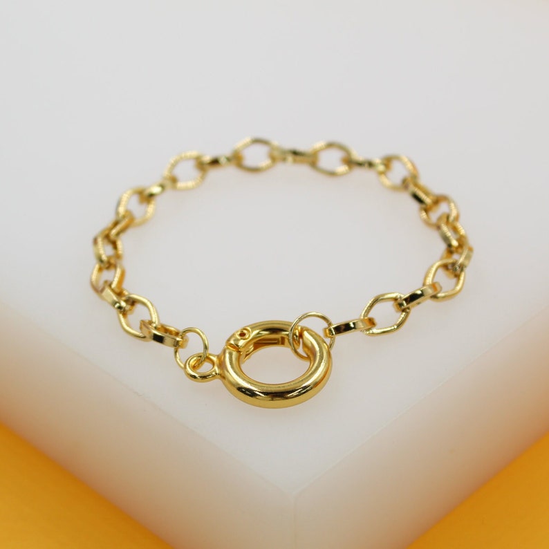 A delicate gold chain bracelet features an eye-catching round spring ring clasp, resting gracefully on a white display surface.