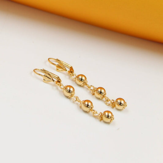 A pair of elegant gold-plated dangle earrings featuring graduated spherical beads rests on a smooth white surface.